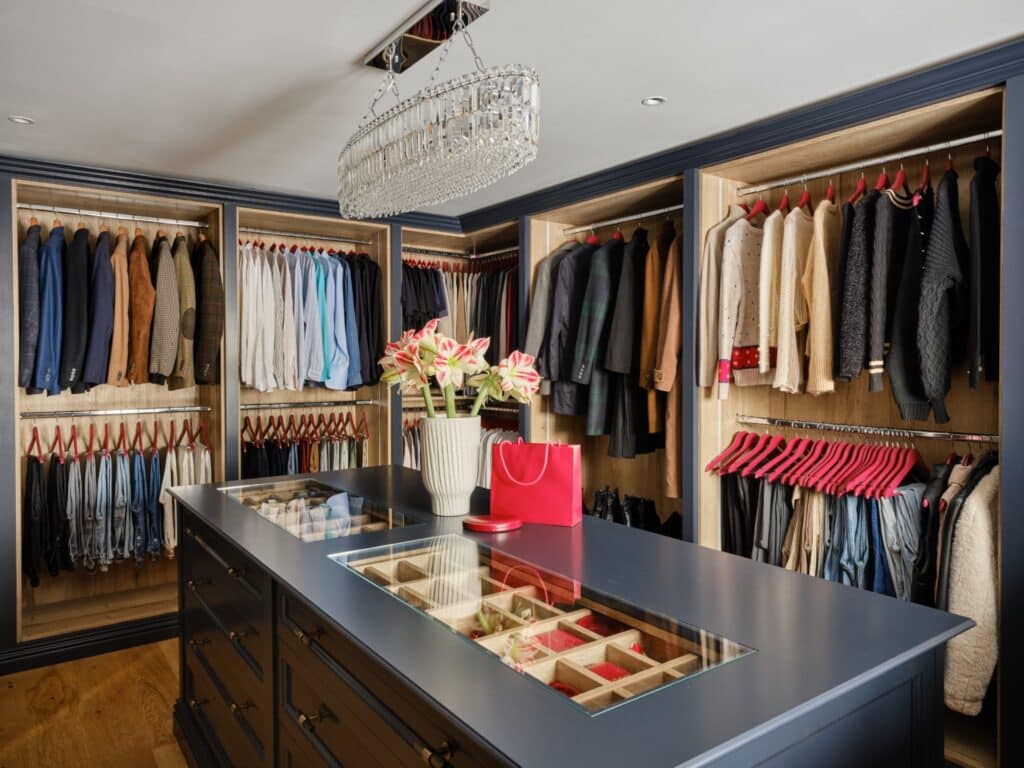 Open fronted bespoke walk-in wardrobe with glass-topped island and internal lighting