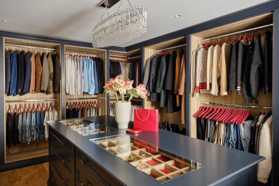 Open fronted bespoke walk-in wardrobe with glass-topped island and internal lighting
